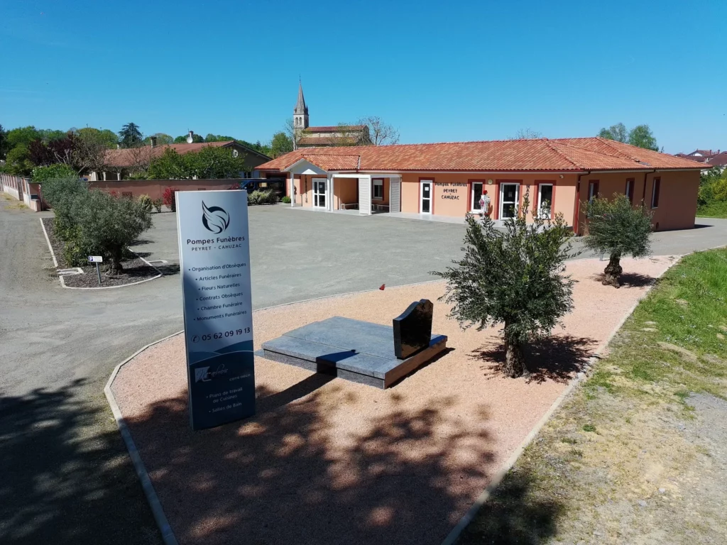 Vue extérieure des Pompes Funèbres Peyret-Cahuzac avec totem d'affichage, parking et monument funéraire en exposition.