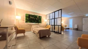 Grand salon funéraire lumineux avec lit de repos, mur végétal décoratif et fauteuils jaunes modernes.