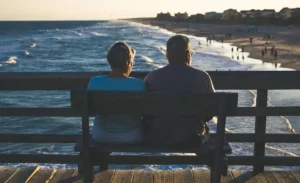 Couple senior assis sur un banc en bois face à la mer et au coucher du soleil.
